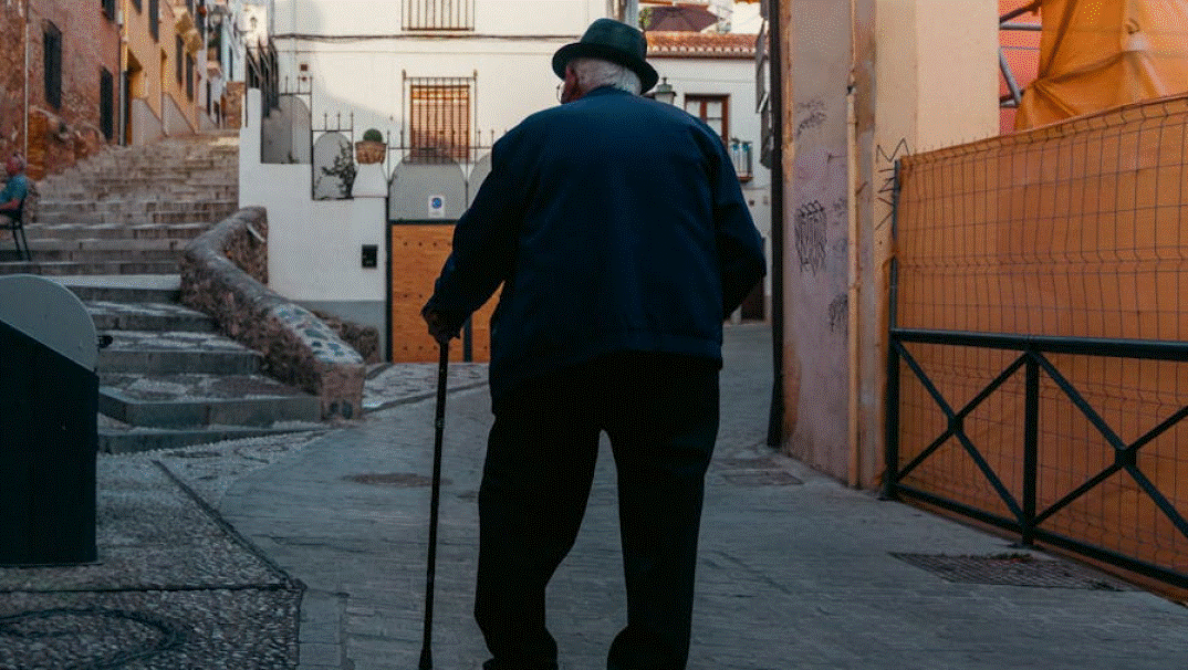 Ηλικιωμένος με μπαστούνι περπατά σε πλακόστρωτο δρόμο οικισμού
