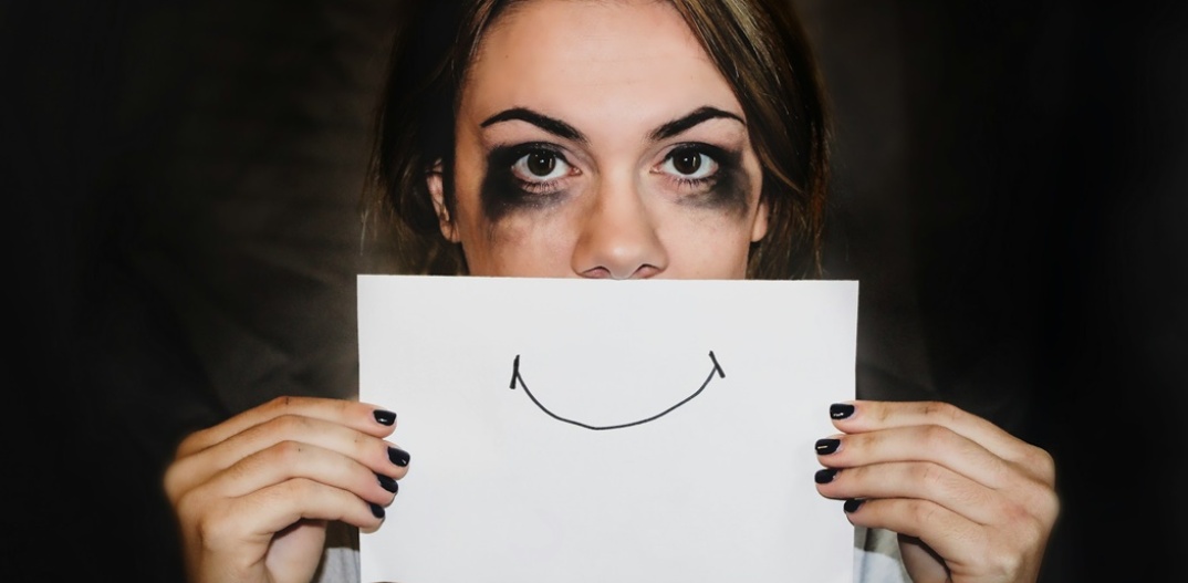 Γυναίκα που κρύβει την κακοποίησή της πίσω από ένα χαρτί με ζωγραφισμένο ένα χαμόγελο