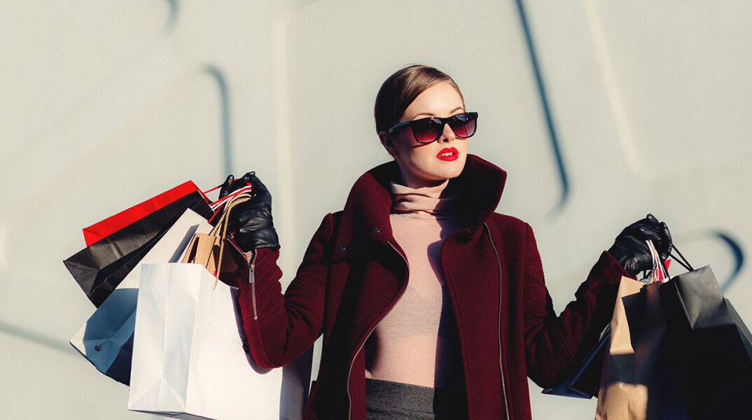 Γυναίκα με γυαλιά ηλίου κρατάει σακούλες αγορών και στα δύο χέρια