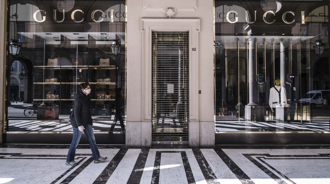 Γυναίκα με μάσκα περπατάει έξω από ένα κλειστό κατάστημα Gucci