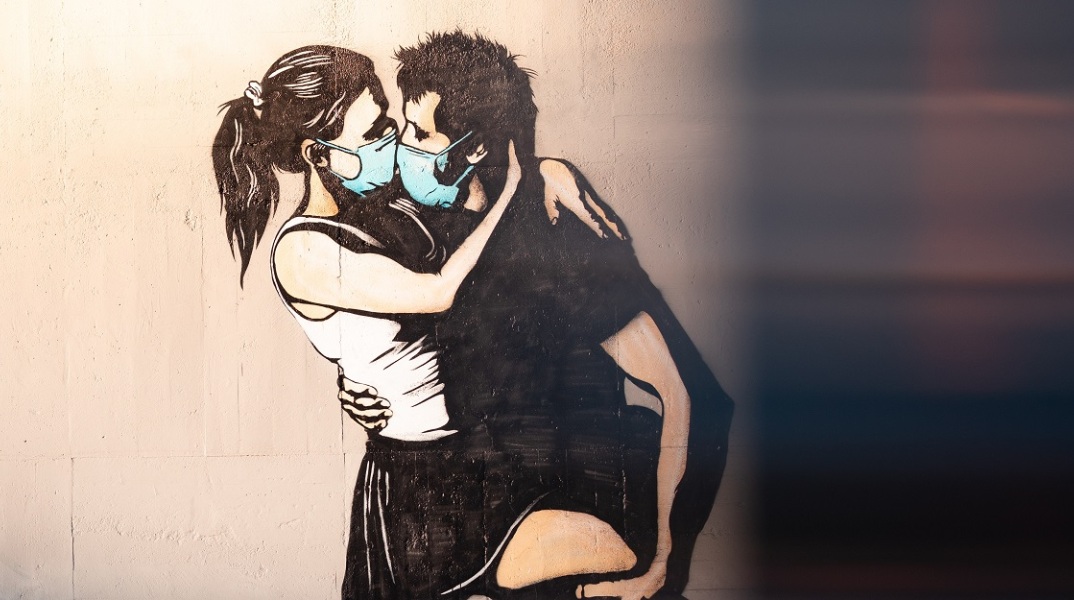 Γκράφιτι με ζευγάρι που φιλιέται φορώντας χειρουργικές μάσκες