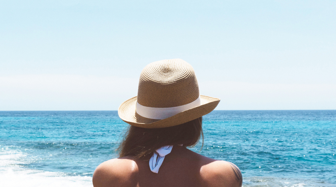 Γυναίκα με ψάθινο καπέλο κοιτάζει τη θάλασσα