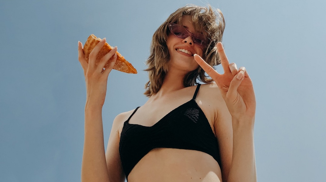 Κοπέλα με γυαλιά ηλίου κρατάει κομμάτι πίτσας