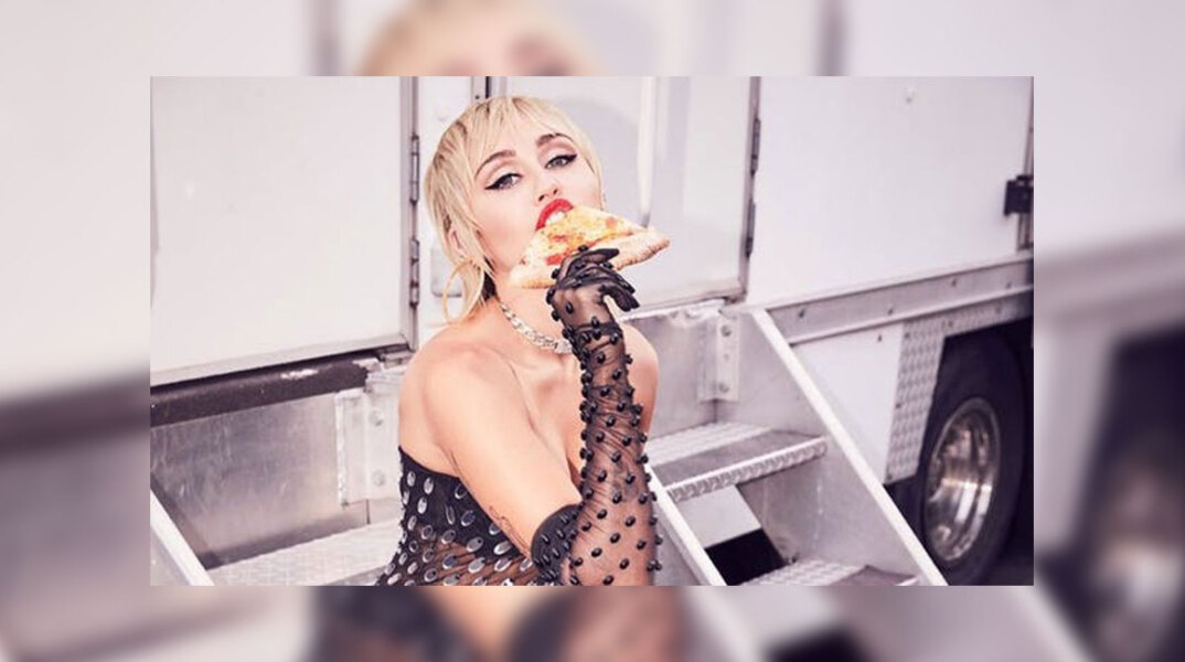 Η τραγουδίστρια Miley Curys με ένα κομμάτι πίτσα στο χέρι της