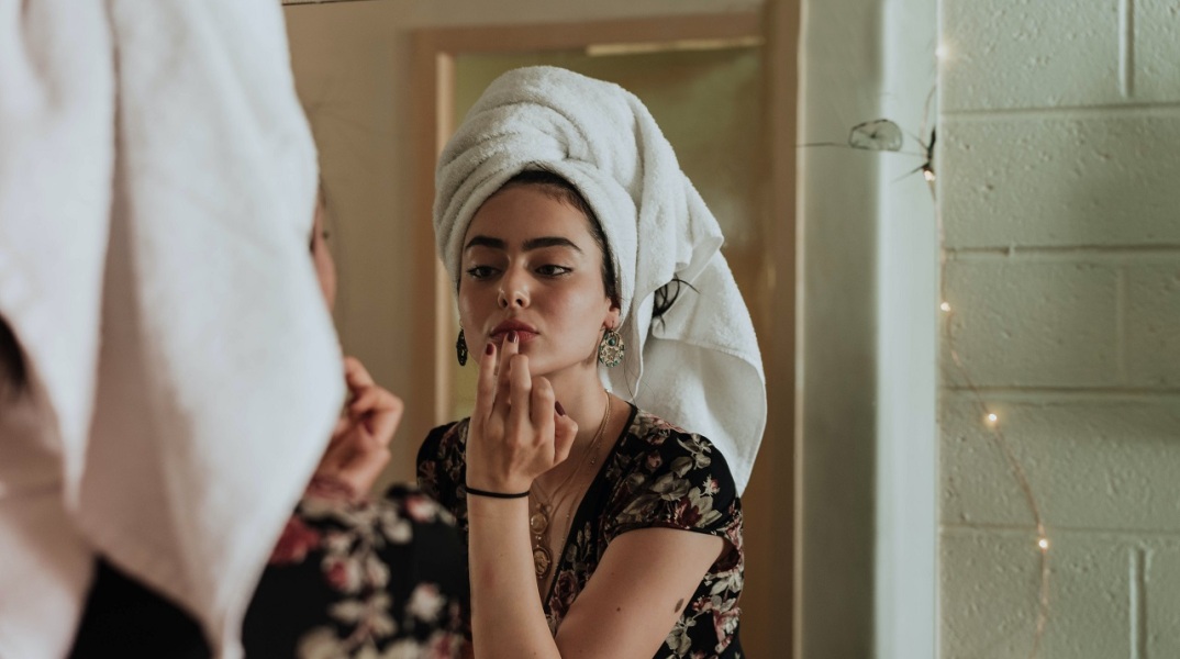 Κοπέλα με πετσέτα στα μαλλιά κοιτιέται στον καθρέφτη