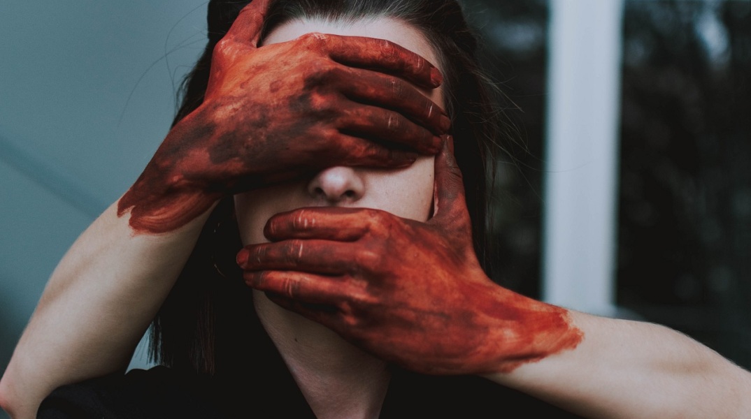 Χέρια με αίματα καλύπτουν πρόσωπο γυναίκας