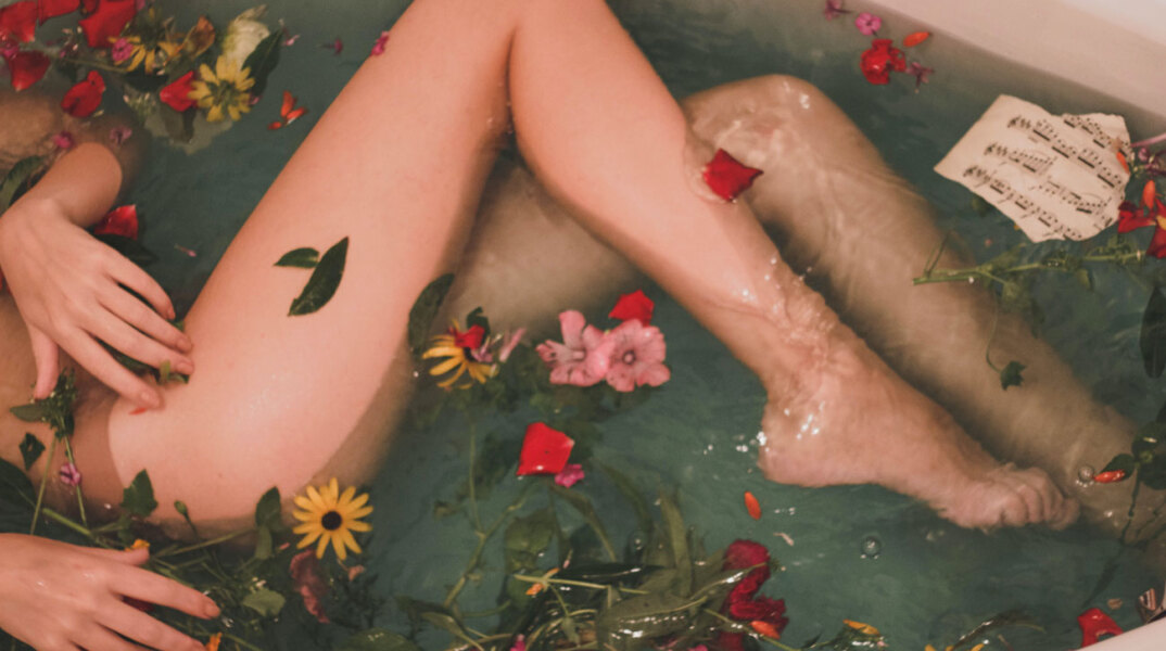 Ξαπλωμένη κοπέλα σε μπανιέρα με νερό και λουλούδια