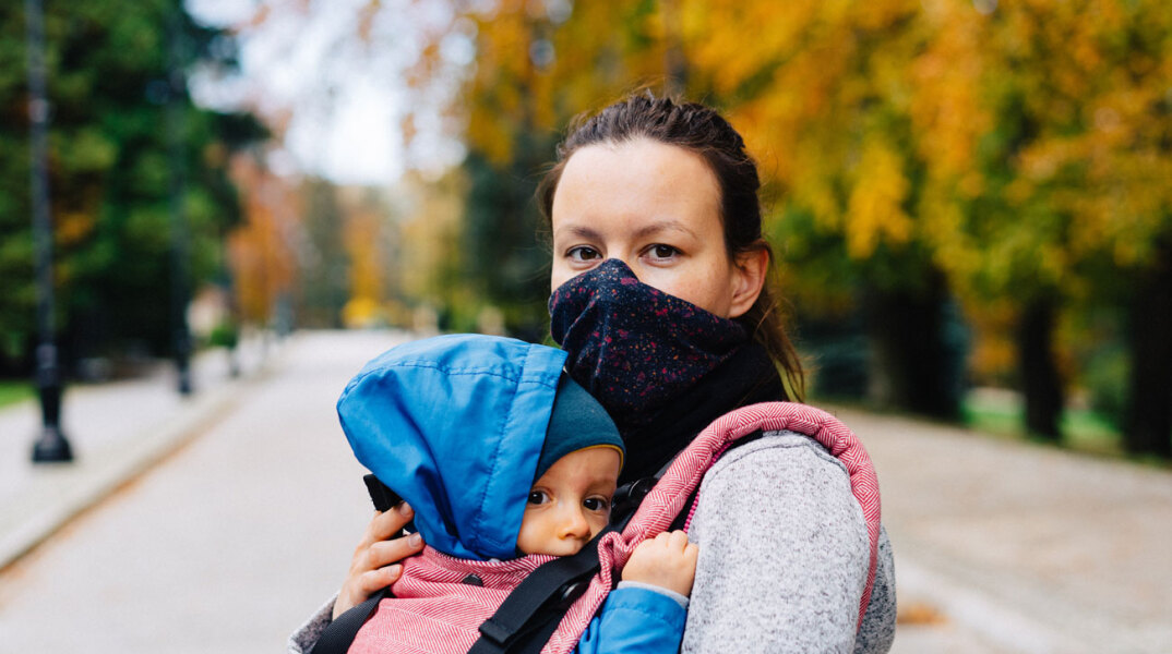 Γυναίκα με μάσκα κρατάει μωρό αγκαλιά