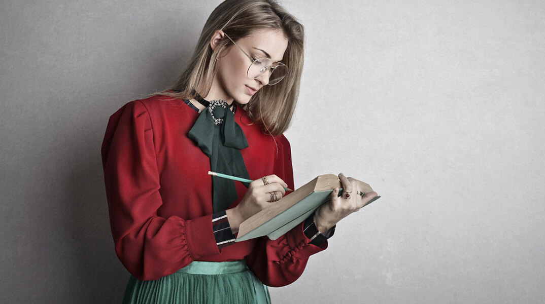 Νεαρή κοπέλα με πράσινη φούστα και κόκκινο πουκάμισο σημειώνει σε βιβλίο