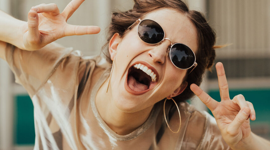 Κοπέλα με γυαλιά ηλίου που γελάει στην κάμερα