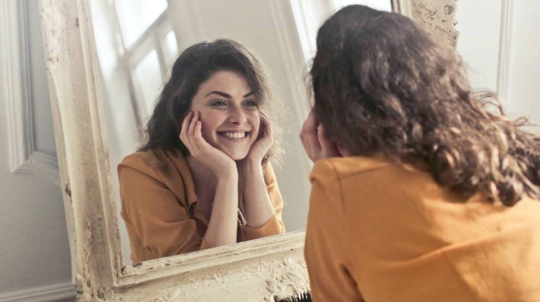 Κοπέλα που κοιτάει στον καθρέφτη και χαμογελάει
