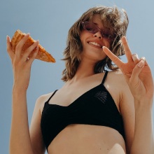 Κοπέλα με γυαλιά ηλίου κρατάει κομμάτι πίτσας