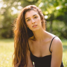 Γυναίκα με μακριά καστανά μαλλιά και μαύρη μπλούζα με τιράντα με φόντο δέντρα