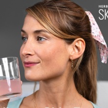 Κοπέλα με μαλλιά αλογοουρά σηκώνει ποτήρι με ροζ υγρό κοντά στο πρόσωπό της