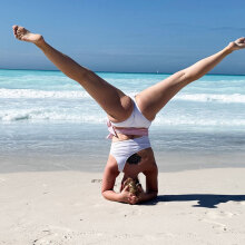 Γυναίκα με άσπρο μαγιό κάνει κατακόρυφο στην παραλία