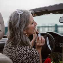 Γκριζομάλλα γυναίκα σε αυτοκίνητο βάζει κραγιόν στον καθρέφτη