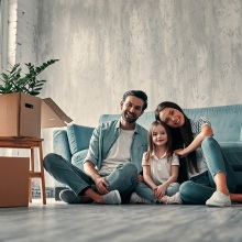 Άντρας, γυναίκα και παιδί καθισμένοι στο πάτωμα σπιτιού με ανοιχτές κούτες τριγύρω