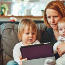 Μια μητέρα κάθεται στον καναπέ αγκαλιά με τα δύο παιδιά της