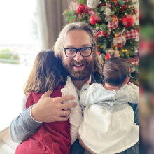 Ο Ευρυπίδης Γουργουλίδης αγκαλιά με τα δύο παιδιά του μπροστά από ένα χριστουγεννιάτικο στολισμένο δέντρο