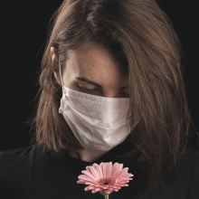 Γυναικά με μάσκα κρατά στα χέρια της ένα λουλούδι