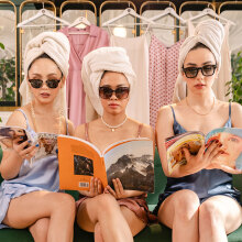 Τρεις γυναίκες με μαύρα γυαλιά ηλίου και πετσέτα τυλιγμένη στο κεφάλι καθισμένες σε καναπέ διαβάζουν περιοδικά