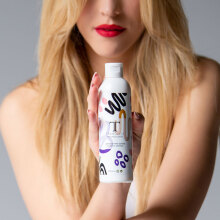 Ξανθιά κοπέλα με κόκκινο κραγιόν ποζάρει καθιστή κρατώντας μπουκάλι Tranoulis