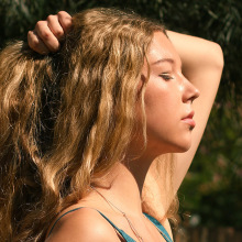 Ξανθιά κοπέλα γυρισμένη προφίλ πιάνει τα μαλλιά της με το ένα χέρι