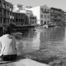 Ασπρόμαυρη φωτογραφία γυναίκας καθισμένης με γυρισμένη την πλάτη και φόντο τη θάλασσα