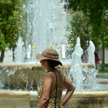 Γυναίκα με καπέλο περπατά εν μέσω καύσωνα δίπλα από το σιντριβάνι της πλατείας Συντάγματος