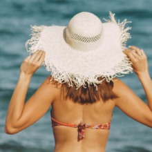 κοπέλα στην παραλία που φοράει μαγιώ και μεγάλο ψάθινο καπέλο 