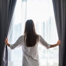 Γυναίκα ανοίγει κουρτίνες σε δωμάτιο