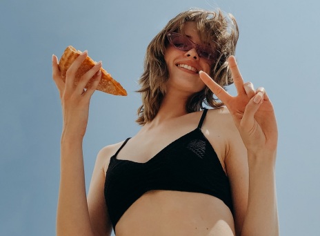 Κοπέλα με γυαλιά ηλίου κρατάει κομμάτι πίτσας