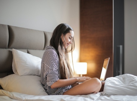 Κοπέλα καθισμένη στο κρεβάτι με ανοιχτό laptop μπροστά της