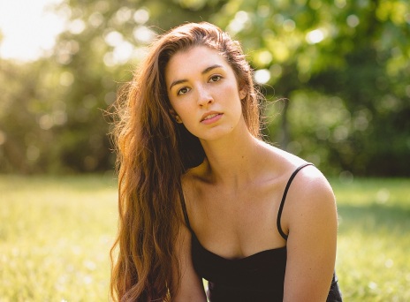 Γυναίκα με μακριά καστανά μαλλιά και μαύρη μπλούζα με τιράντα με φόντο δέντρα