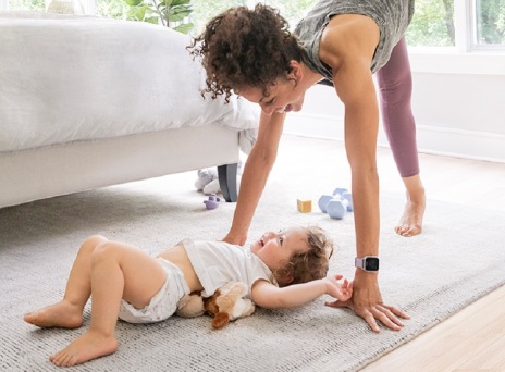 Γυναίκα γυμνάζεται στην κρεβατοκάμαρα δίπλα σε μωρό ξαπλωμένο στο πάτωμα