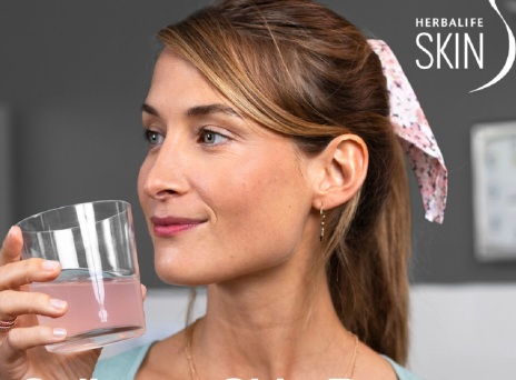 Κοπέλα με μαλλιά αλογοουρά σηκώνει ποτήρι με ροζ υγρό κοντά στο πρόσωπό της