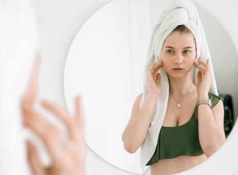 Κοπέλα κοιτάζεται σε καθρέφτη και ακουμπάει το πρόσωπό της