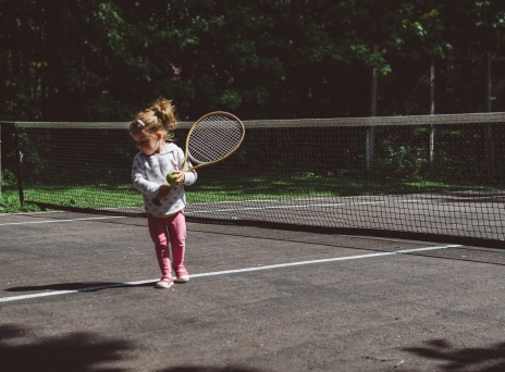 Μικρό κορίτσι σε γήπεδο τένις με μπαλάκι και ρακέτα τένις