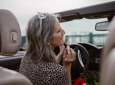 Γκριζομάλλα γυναίκα σε αυτοκίνητο βάζει κραγιόν στον καθρέφτη