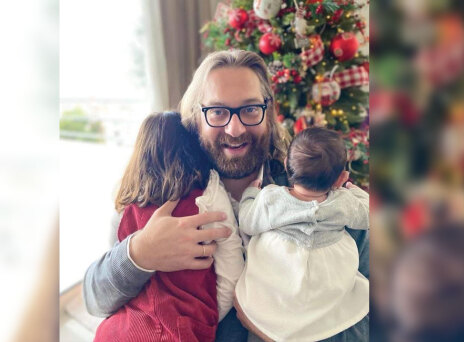 Ο Ευρυπίδης Γουργουλίδης αγκαλιά με τα δύο παιδιά του μπροστά από ένα χριστουγεννιάτικο στολισμένο δέντρο