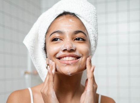 Κοπέλα με πετσέτα στα μαλλιά σαπουνίζει το πρόσωπό της