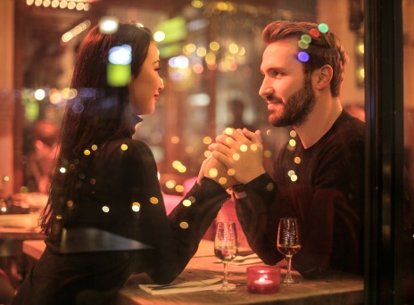 Γυναίκα και άνδρας κρατάνε χέρια καθιστοί σε ένα τραπέζι πίσω από τζαμαρία