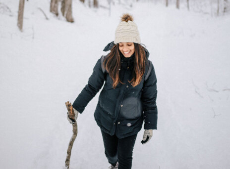 Κοπέλα με μαύρα ρούχα και λευκό σκουφάκι περπατάει στο χιόνι