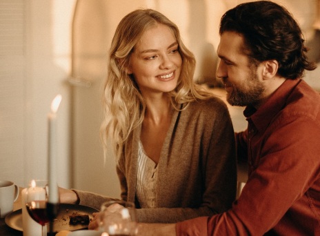 Γυναίκα και άνδρας κοιτάζονται καθισμένοι διπλα δίπλα σε τραπέζι με αναμμένα κεριά