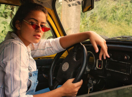 Γυναίκα καθισμένη σε αυτοκίνητο, κρατάει τιμόνι και κοιτάζει την κάμερα