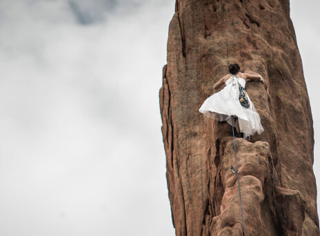 Γυναίκα με λευκό φόρεμα σκαρφαλώνει σε κάθετο βράχο