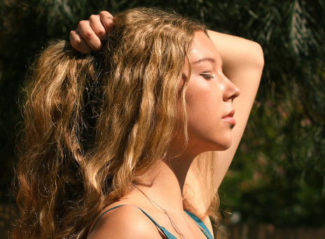 Ξανθιά κοπέλα γυρισμένη προφίλ πιάνει τα μαλλιά της με το ένα χέρι