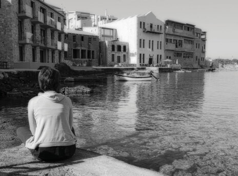 Ασπρόμαυρη φωτογραφία γυναίκας καθισμένης με γυρισμένη την πλάτη και φόντο τη θάλασσα