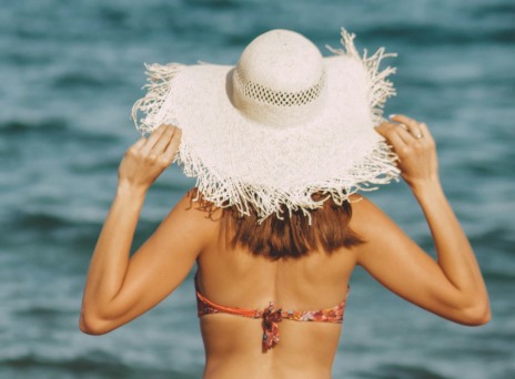 κοπέλα στην παραλία που φοράει μαγιώ και μεγάλο ψάθινο καπέλο 