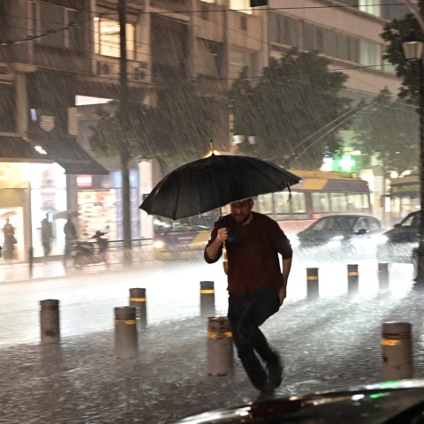 Πολίτης με ομπρέλα εν μέσω καταιγίδες και πλημμυρισμένων δρόμων